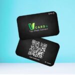 Two VCards floating against a light blue background, showcasing the front and back sides. The front displays the VCard logo with the words "Tap, Share, Connect" and an NFC symbol, while the back features a QR code and the website URL "www.vcarde.com."