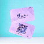 Purple NFC card with QR code floating in front of a turquoise background. The card features the text: "V Card - Tap, Share, Connect" along with an ID number and the URL "www.vcarde.com."